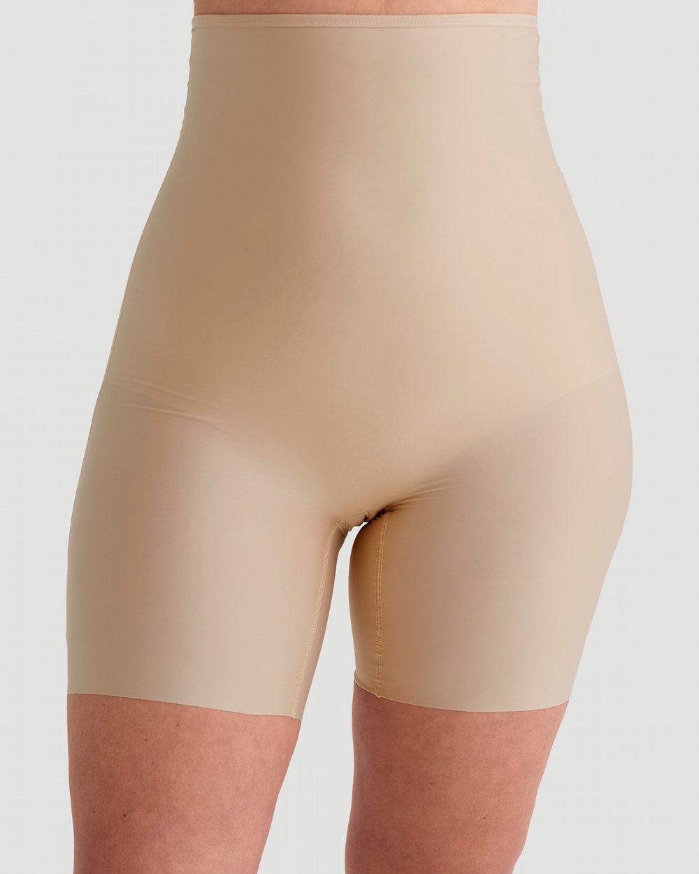 A person wearing high-waisted, nude-colored shapewear shorts against a plain background.