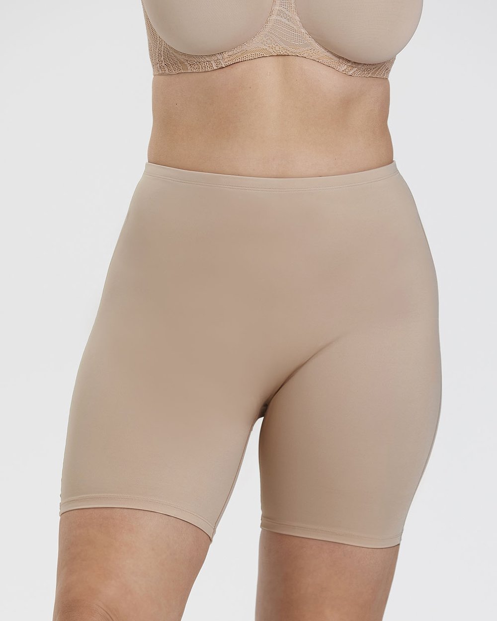 Person wearing beige high-waisted shapewear shorts and a lace bra, standing against a plain white background.