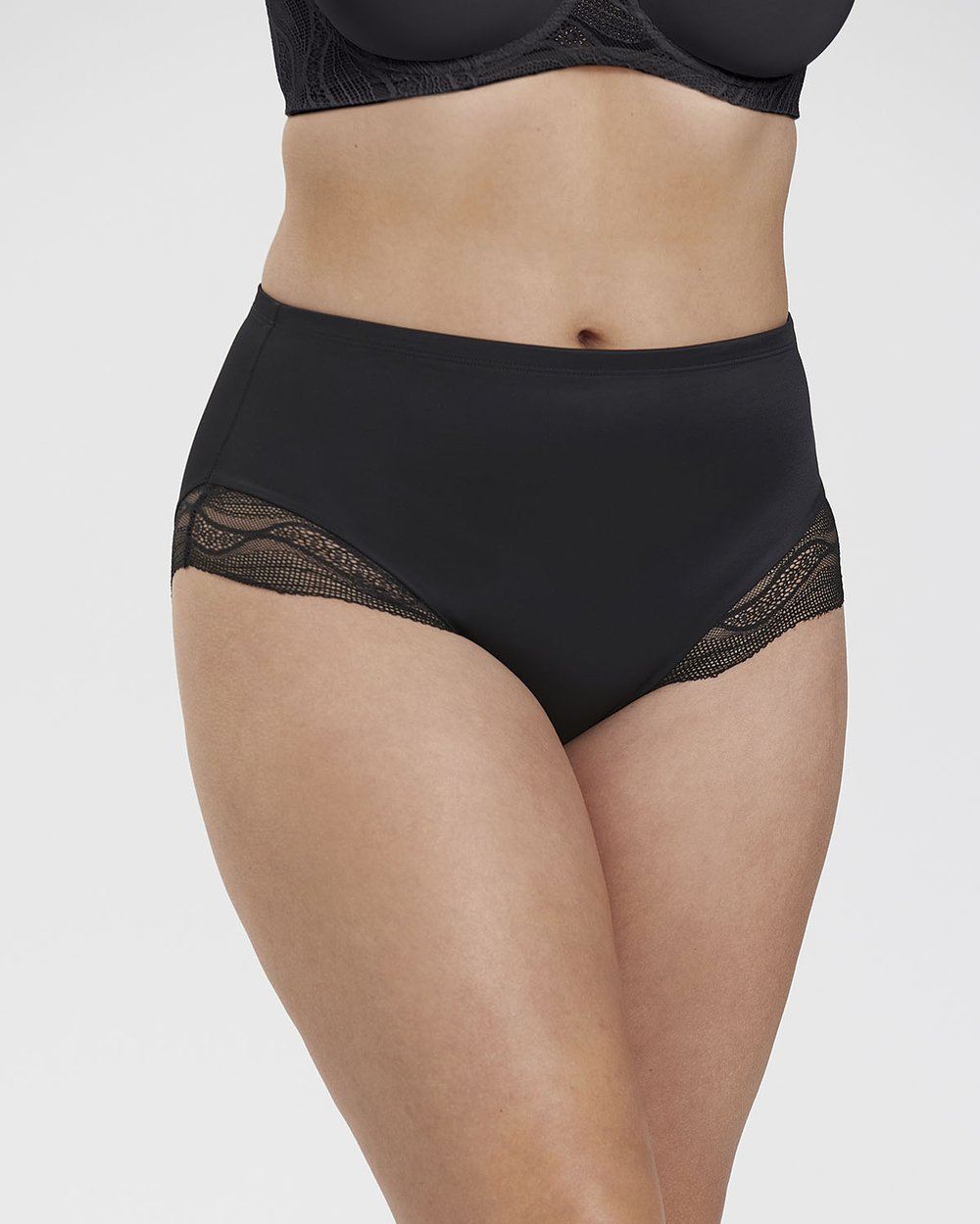 A person wearing high-waisted black underwear with lace trim, paired with a matching black bra, against a plain background.