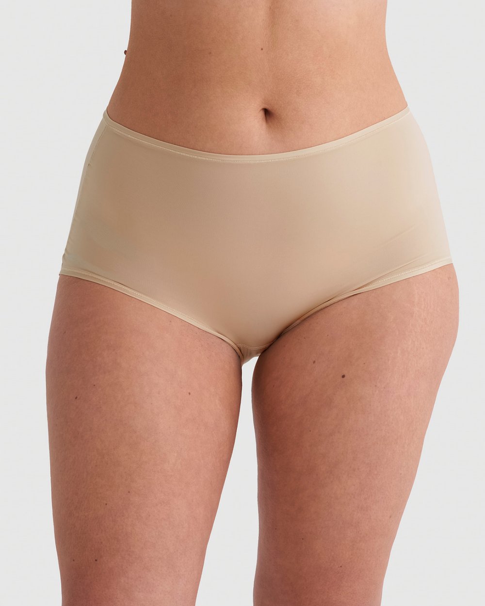 Person wearing high-waisted, nude-colored underwear, standing against a white background.