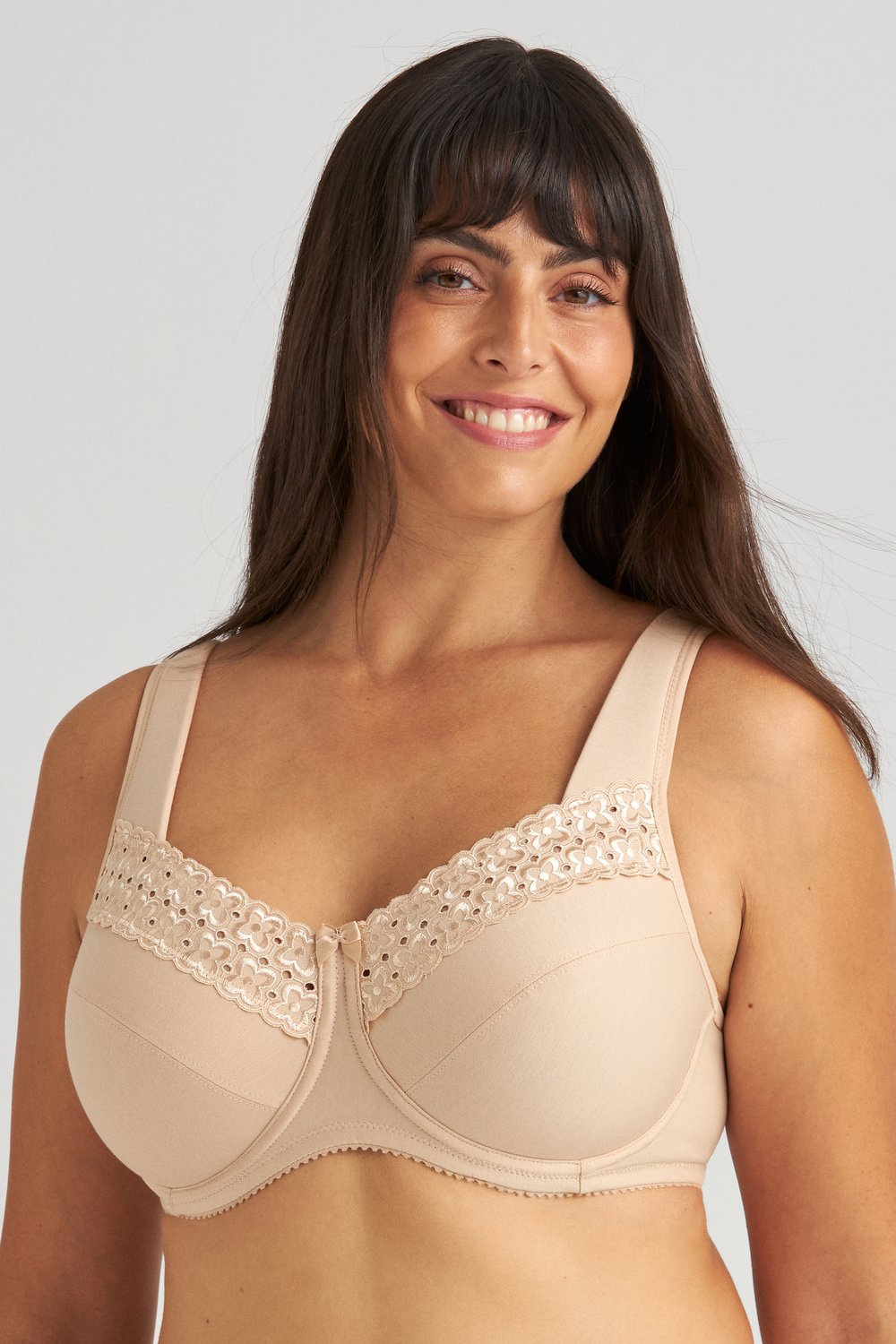 Smiling woman wearing a beige bra with floral lace details, standing against a light background.
