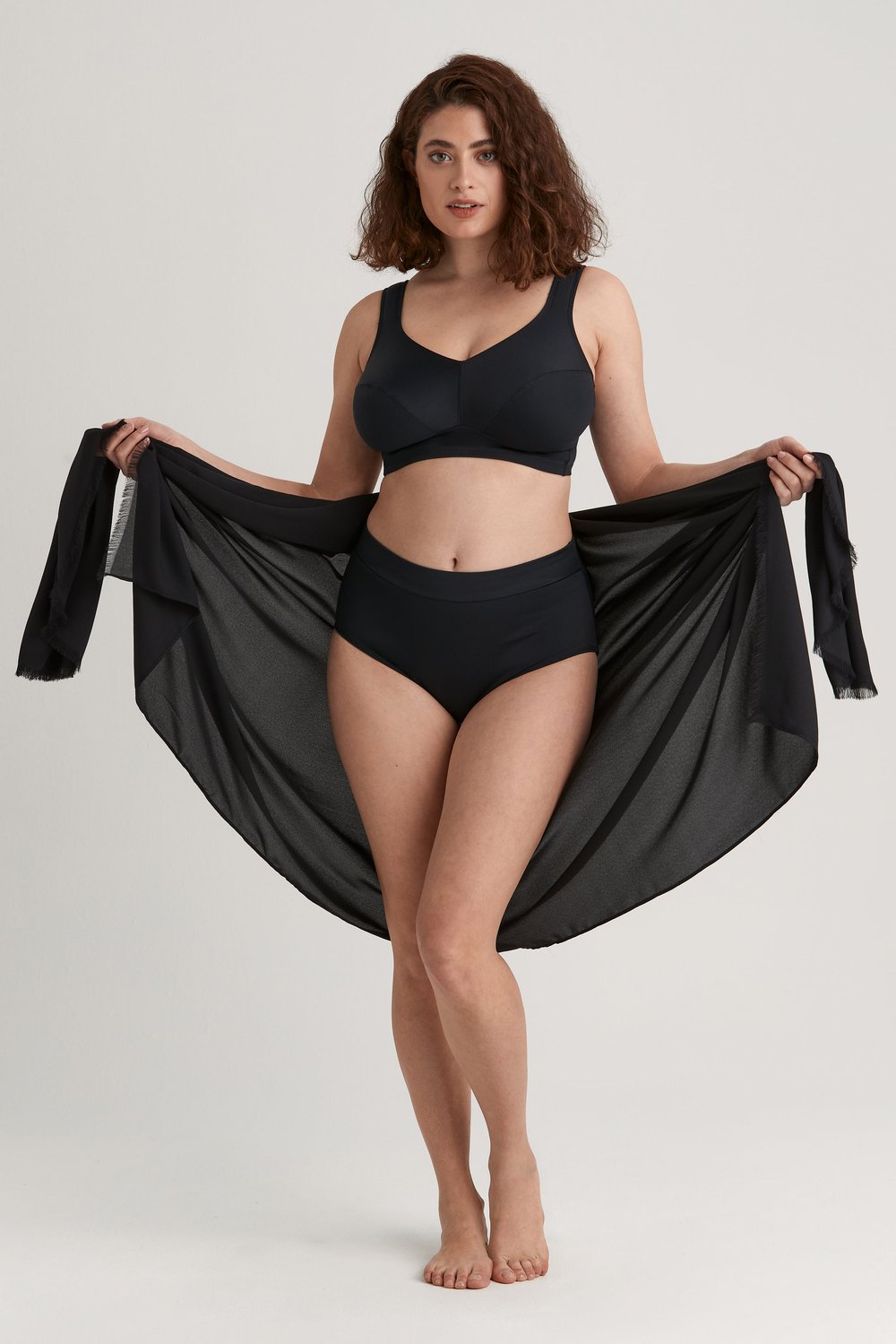 Femme tenant ouvert un sarong léger noir Miss Mary aux bords frangés, porté avec un maillot de bain noir.