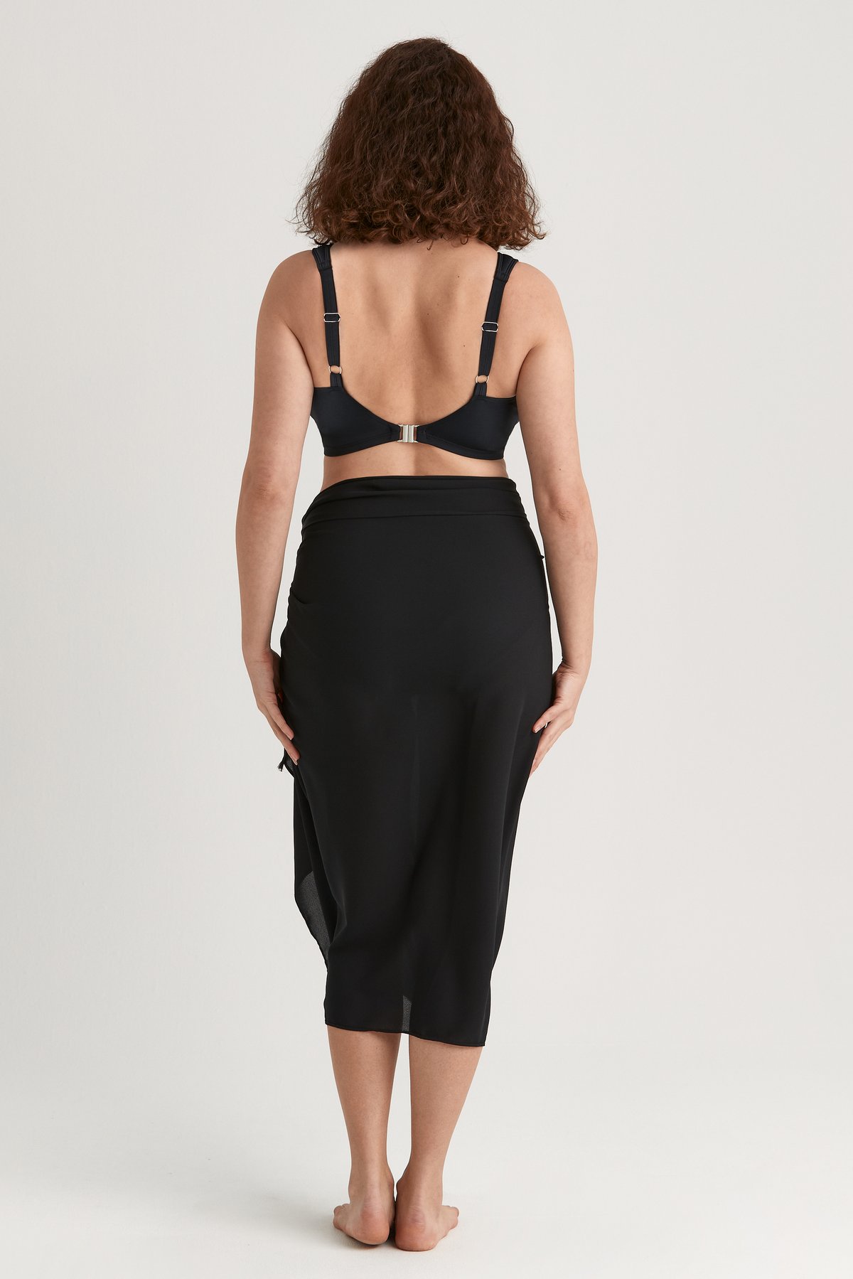 Vue de dos d'une femme portant un sarong léger noir Miss Mary noué autour de la taille.