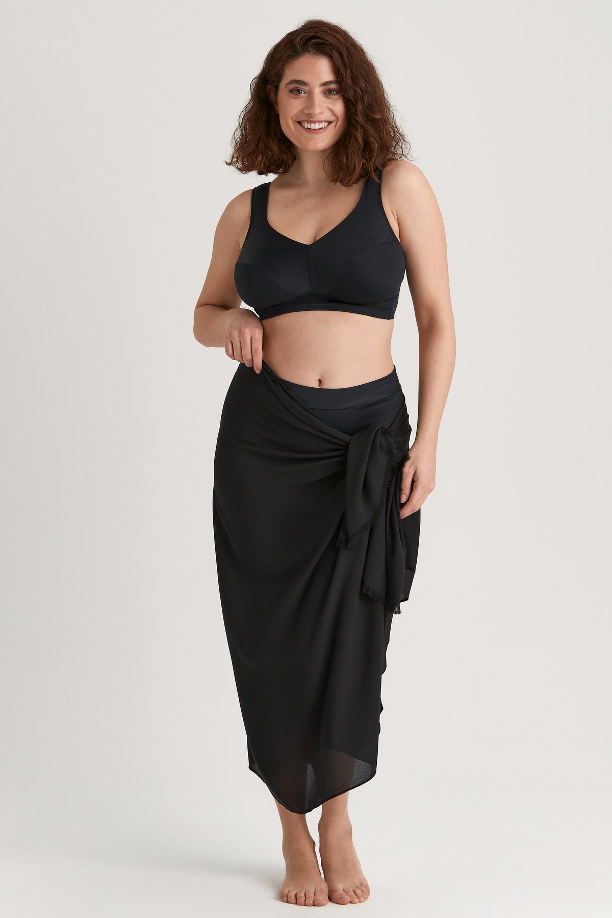 Femme souriante portant un sarong léger noir Miss Mary noué autour de la taille en jupe.