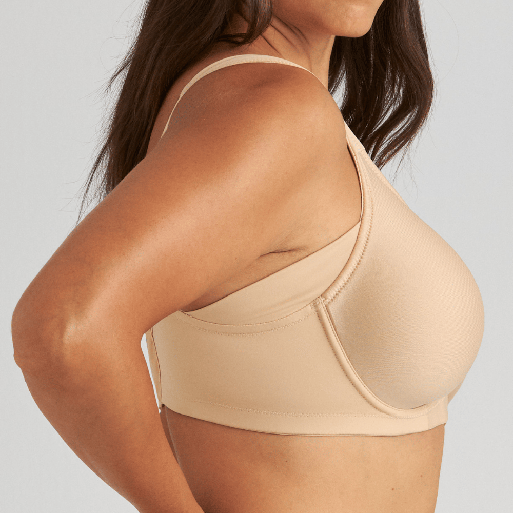 A woman in a beige bra is shown in a side profile with her hands on her hips, against a plain background.