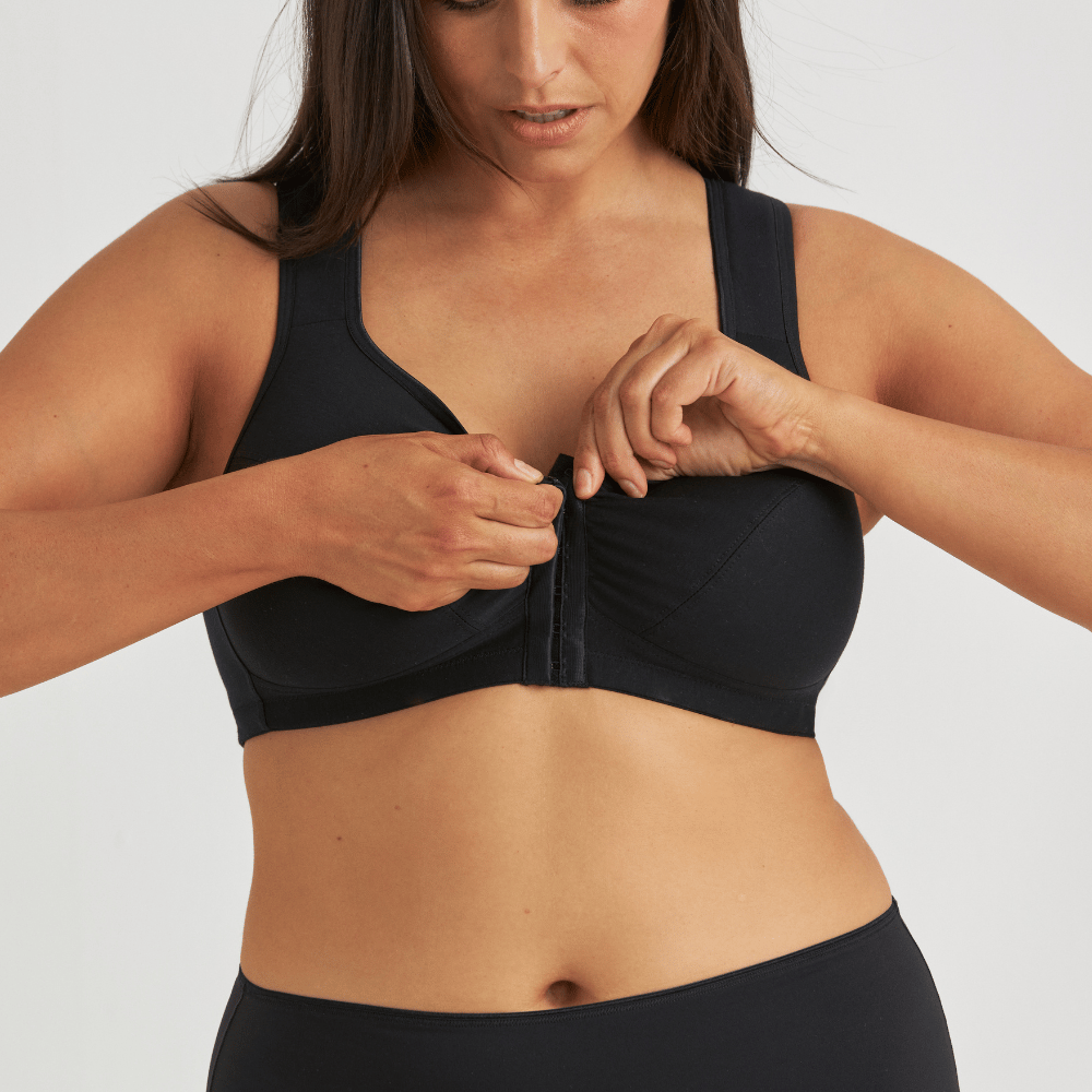 A woman wearing a black front-closure sports bra adjusts the clasp.
