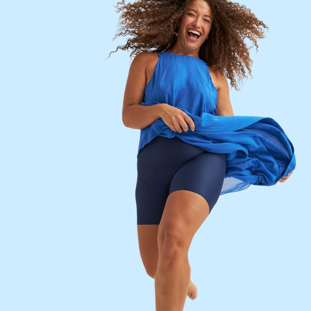 Person in a blue outfit joyfully smiling and running, with wind blowing through their curly hair against a light blue background.