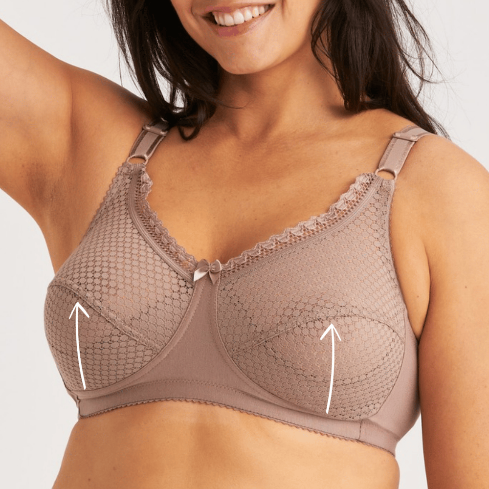 A woman wearing a beige lace bra with embroidered patterns and small bows, raising one arm and smiling. Arrows point to areas on the cups.