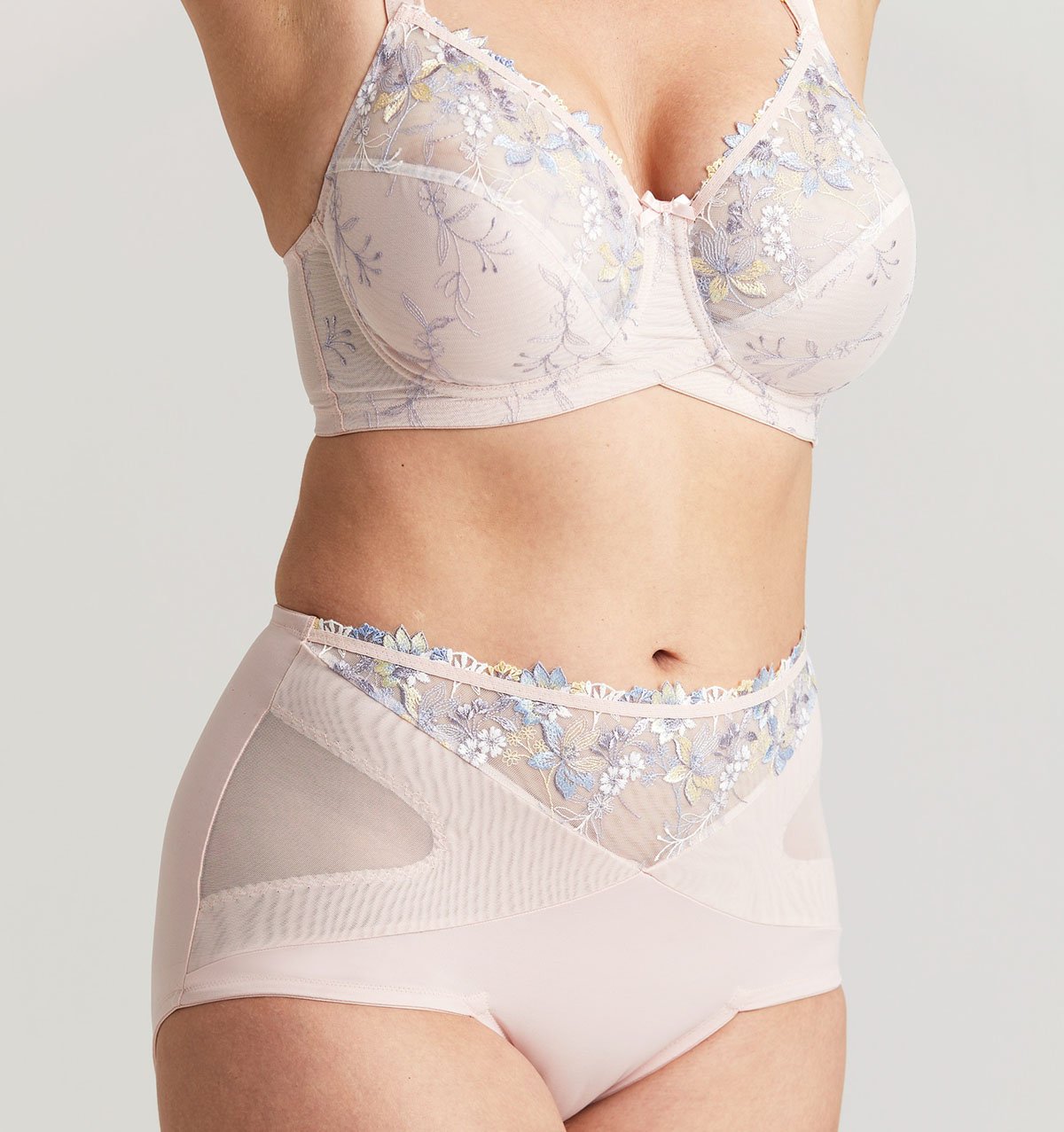 Close-up torso wearing a pale blush bra and high‑waist briefs with pastel floral embroidery and sheer mesh panels.