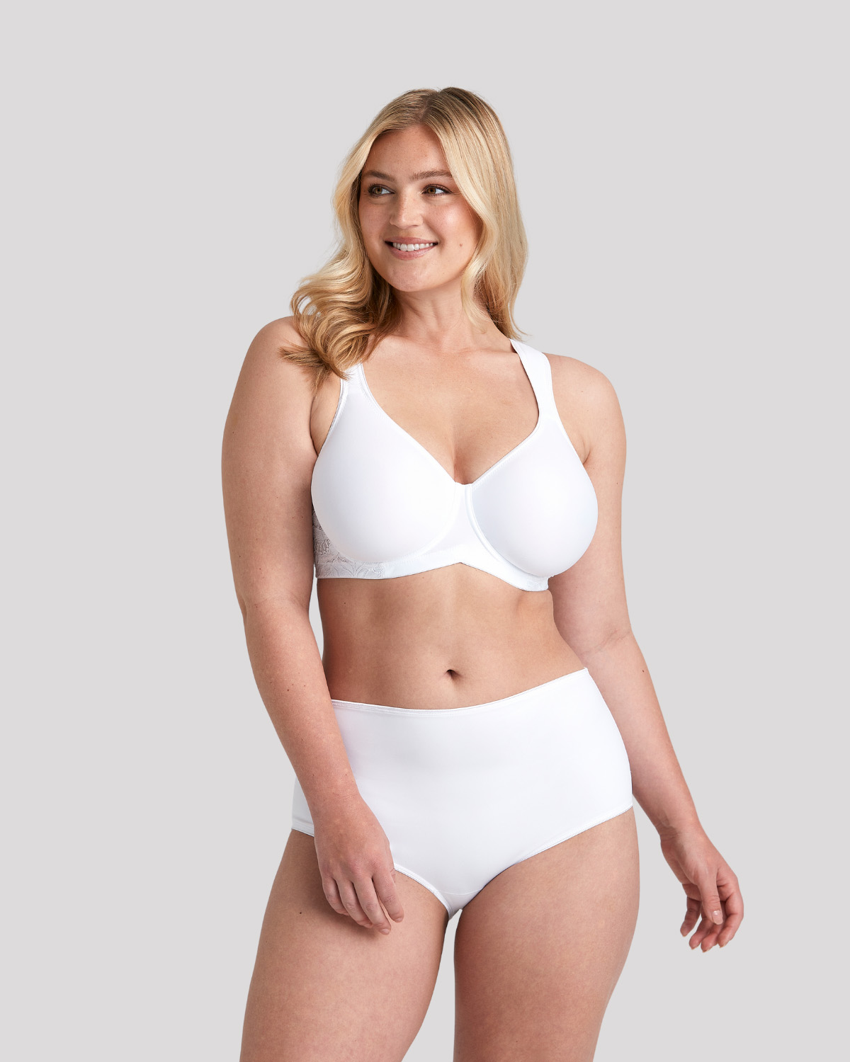 Smiling blonde woman modeling a white full-coverage bra and high‑waist briefs against a light gray background.
