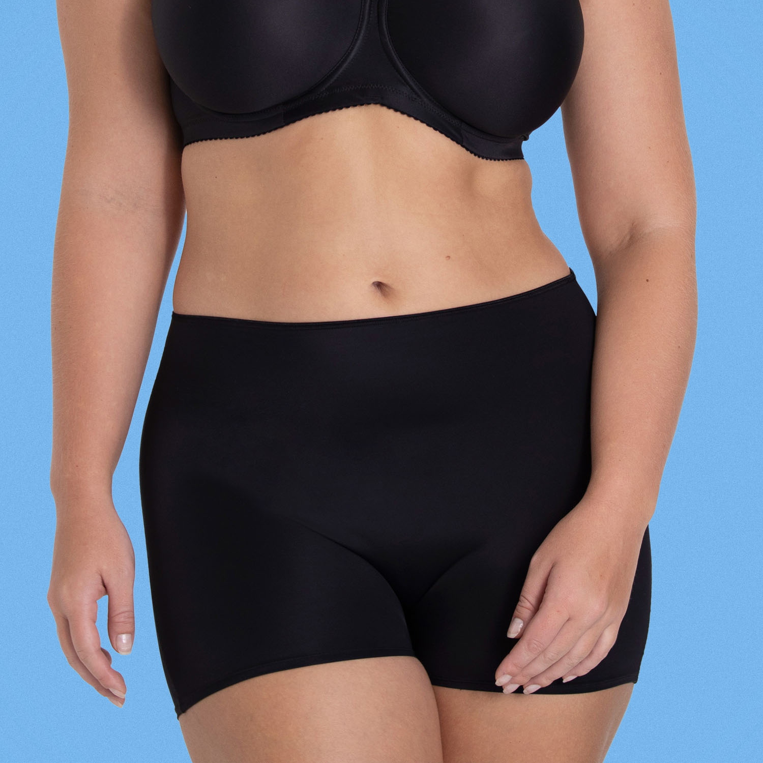 Person wearing a black bra and high-waisted black shorts against a blue background.