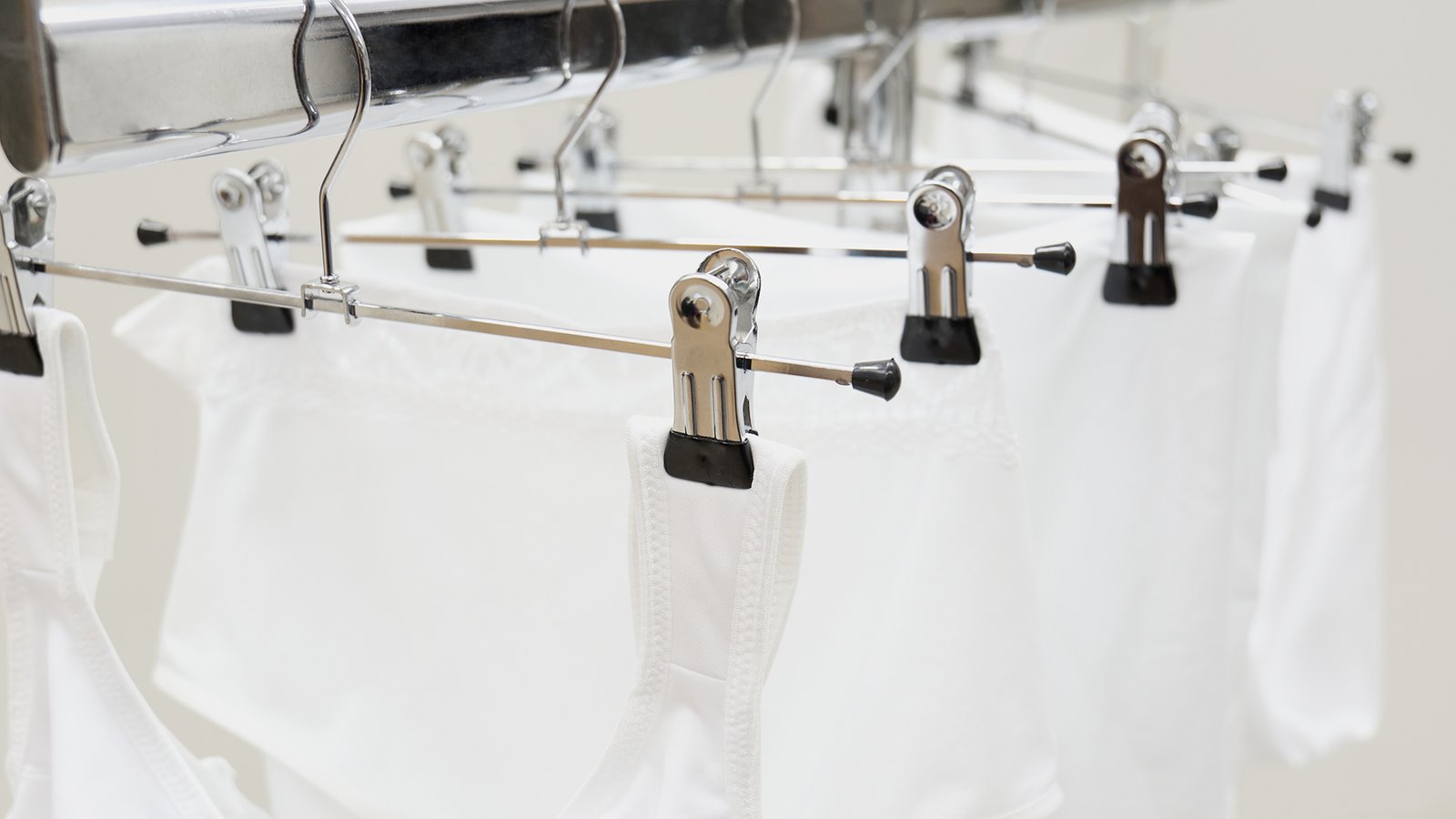 White garments hung on metal hangers with clips, drying indoors on a horizontal rod.