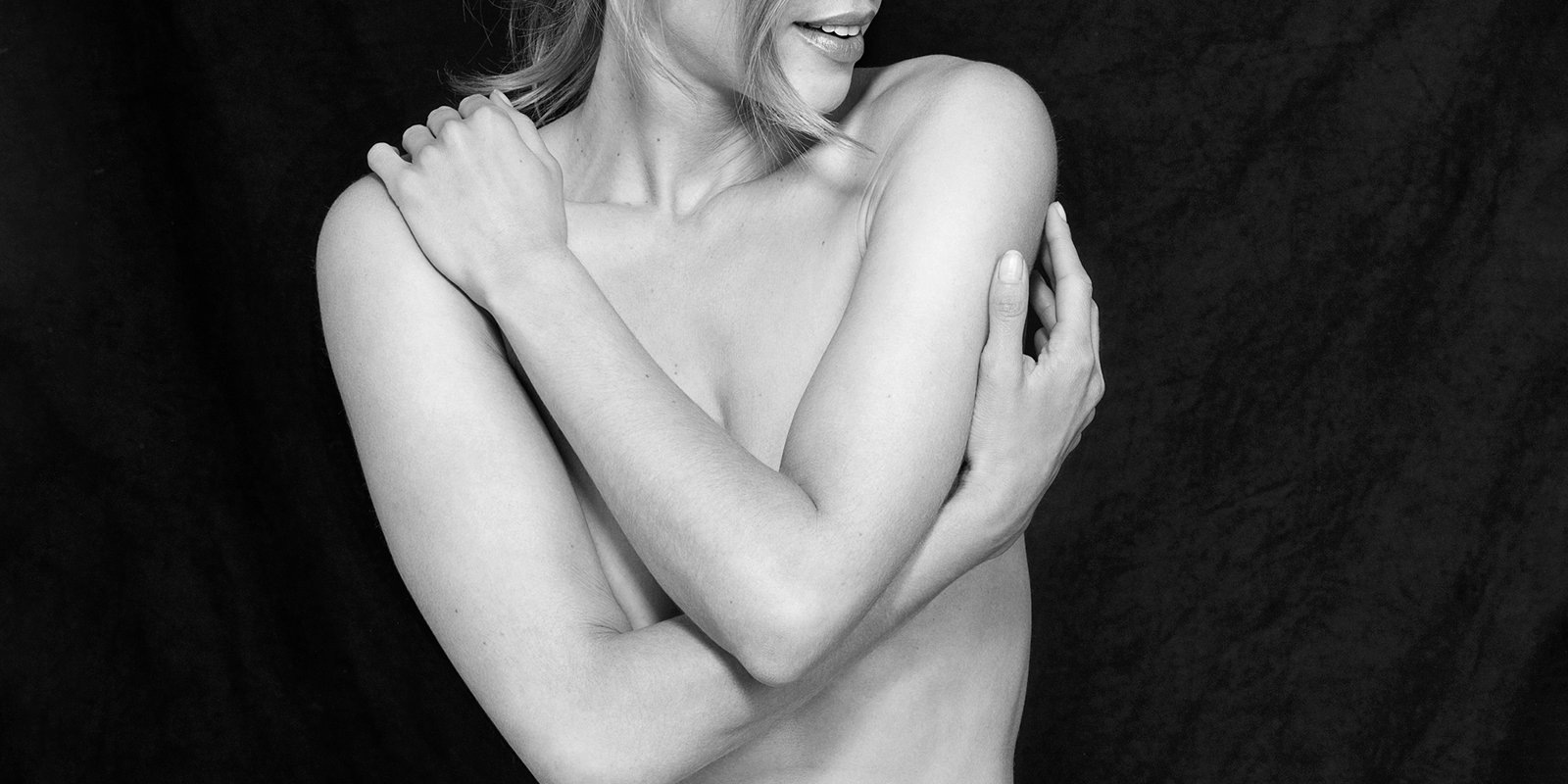 Black and white image of a person with crossed arms over their chest, smiling slightly against a dark backdrop.